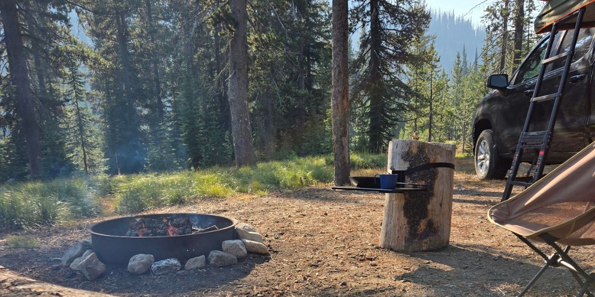 Top Shelf outdoor and camping table mounted to a tree stump in a campsite holding cooking pots and pans.