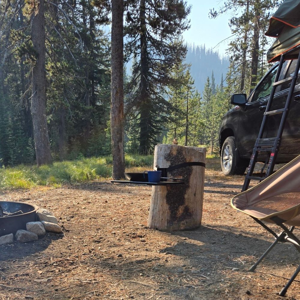 Top Shelf outdoor and camping table mounted to a tree stump in a campsite holding cooking pots and pans.